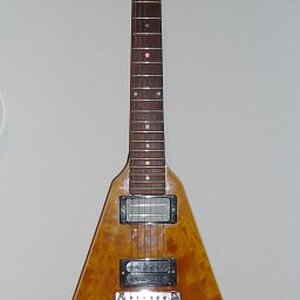 Fred V

Diese eigentlich originale 70er Jahre Gibson Flying V wurde extrem modifiziert. Das 70er Jahre Design lässt viel Platz zwischen Korpus-Oberfläche und Griffbrett Oberkante. Also hatte jemand die Idee, eine schöne Decke aufzukleben. Der Korpus ist nun von einem Binding eingefasst und die Tunomatic Brücke durch einen Wraparound-Steg ersetzt worden.
Ich habe sie von einem Gitarristen namens "Fred" bekommen, deswegen heisst das Teil bei mir immer die "Fred Vee". Er hat sie mir gegen ein Päckchen Saiten überlassen. Allerdings war sie da komplett nackt und die Kopfplatte abgebrochen. Aber damit hatte ich ja schon Erfahrung und hab mit einer dünnen Lage Glasfaser abgeholfen, Die Stelle ist nun etwas rau, aber es wurd keine deckende Neulackierung nötig, was ja auch sehr schade gewesen wäre.
Die Pickups sind welche, die ich zu der Zeit aus anderen Gitarren ausgebaut hatte, weil sie mir dort nicht gefielen. Hier machen sie aber eine gute Figur: ein SH-8 "Invader" und ein OBL.
